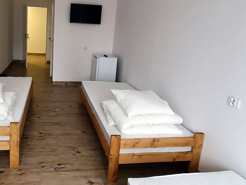 Hotel pracowniczy w Warszawie, pokój 3-osobowy: pokój trzyosobowy z drewnianymi łóżkami, białą pościelą, telewizorem i małą lodówką